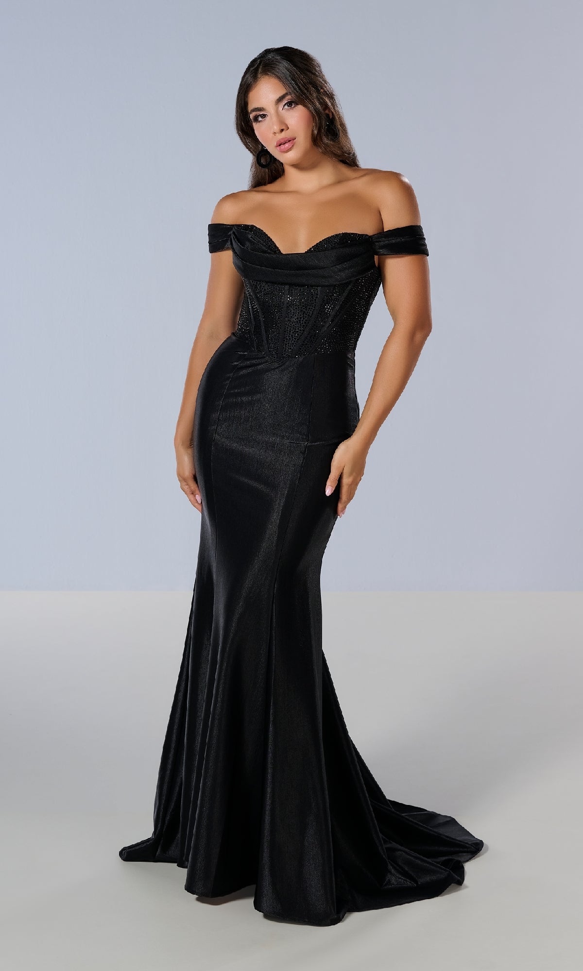 A woman stands against a plain light background wearing the Tiffany 16193 long prom dress, featuring an off-the-shoulder design, fitted silhouette, structured bodice, and floor-length style.